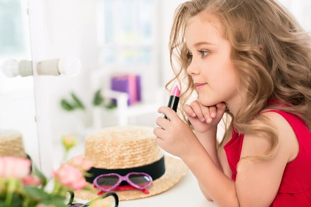 鏡の近くに座っている化粧品を持つ少女。