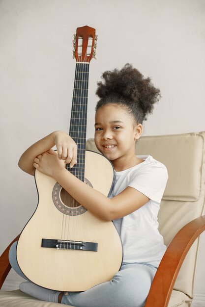 Little girl with curly hair. Learning to play guitar. Little girl in a chair.