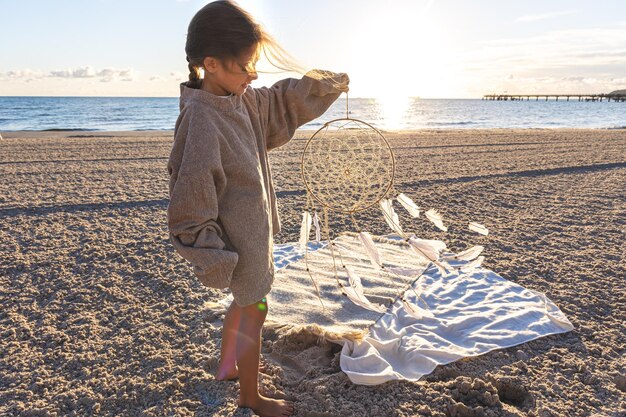 Little girl with a dream catcher on the seashore at sunset