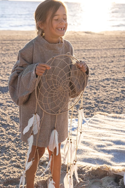Free photo little girl with a dream catcher on the seashore at sunset