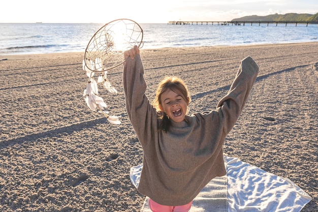 Foto gratuita bambina con un acchiappasogni in riva al mare al tramonto