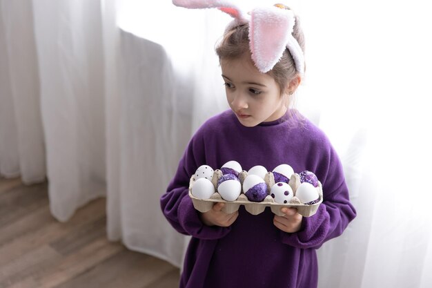 A little girl with easter ears holds a tray of holiday eggs