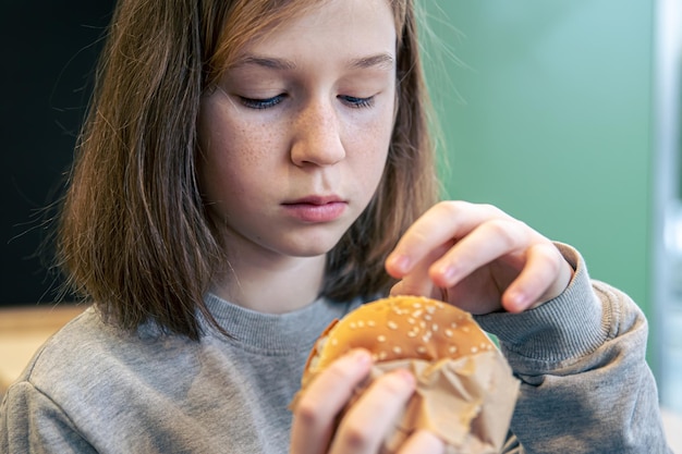 A little girl with freckles eats a burger