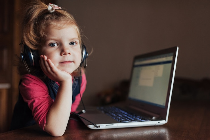 Free Photo little girl with headphones listening to music, using laptop