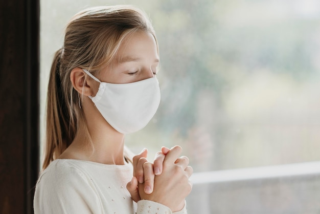 Bambina con la mascherina medica che prega