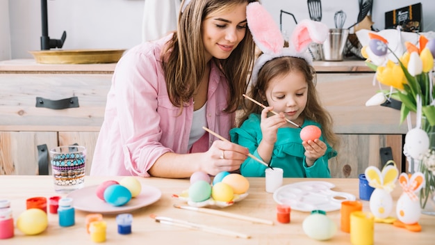 Bambina con uova di pittura madre per pasqua