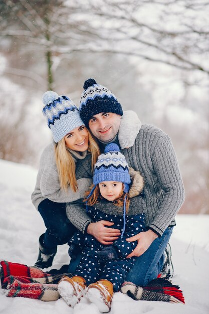 Маленькая девочка с родителями сидит на одеяле в зимнем парке