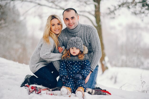 Маленькая девочка с родителями сидит на одеяле в зимнем парке