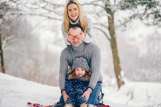 Little girl with parents sitting on a blanket in a winter park