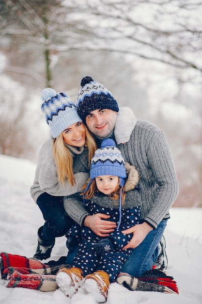 Бесплатное фото Маленькая девочка с родителями сидит на одеяле в зимнем парке