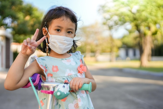 Little girl with protective face mask playing scooter outdoor