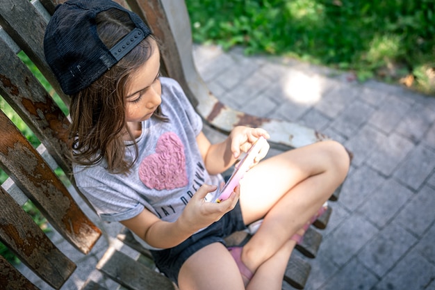 Bambina con smartphone in un berretto all'aperto in estate.