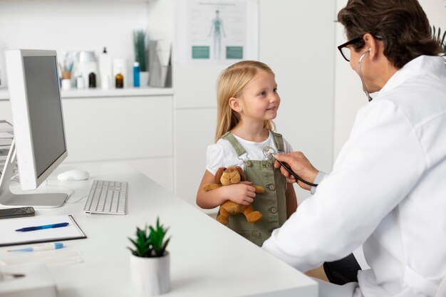 Маленькая девочка с игрушкой плюшевый мишка на приеме у врача