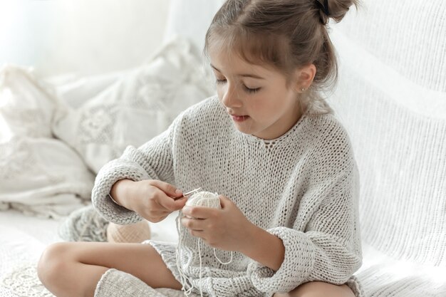 Little girl with threads learns to crochet, home leisure and needlework.