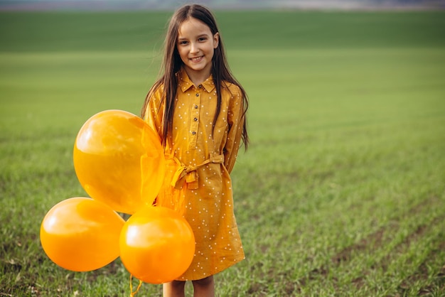 Маленькая девочка с желтыми воздушными шарами в поле