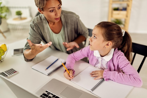 Little girl writing homework while mother is trying to explain her the assignment