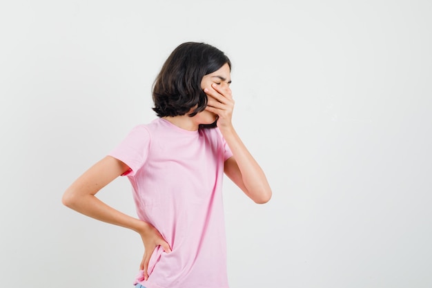 Little girl yawning in pink t-shirt and looking sleepy , front view.