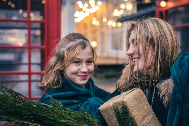 A little girl and young woman with thuja branches and a gift under a plaid