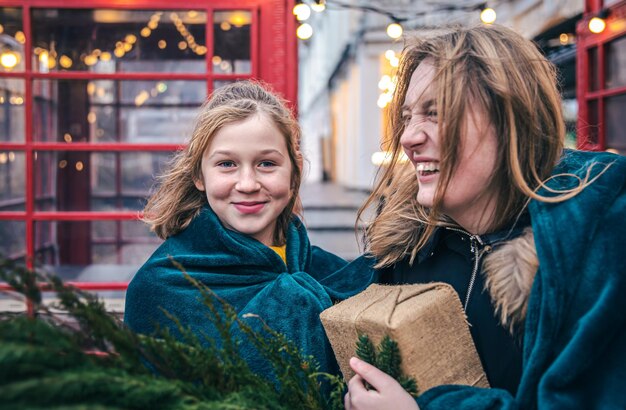 A little girl and young woman with thuja branches and a gift under a plaid