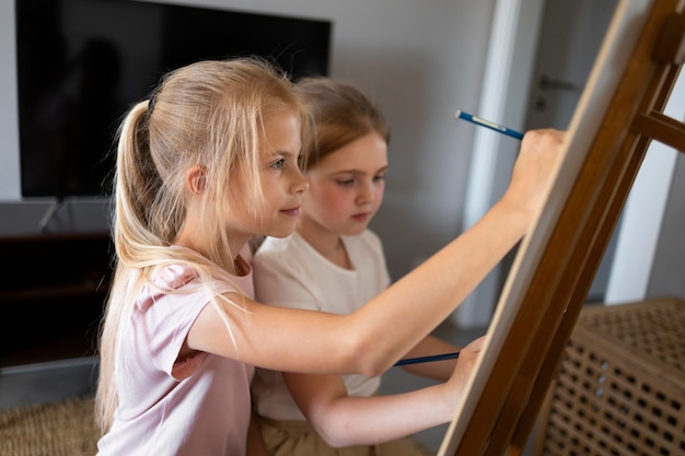 Free photo little girls drawing using easel at home together