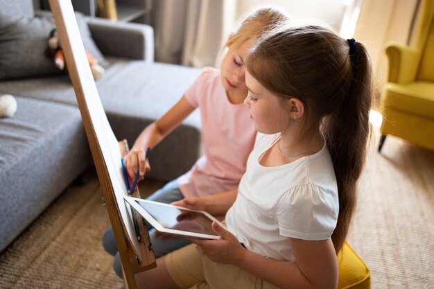 Little girls drawing using easel and tablet at home