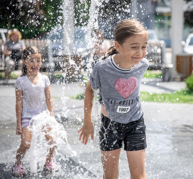 Little girls play in a fountain among splashes of water.