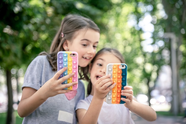 Little girls use phones in trendy cases for anti stress pop it.
