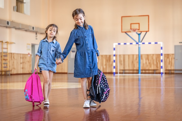 Free photo little girls with backpacks in an empty school gym.