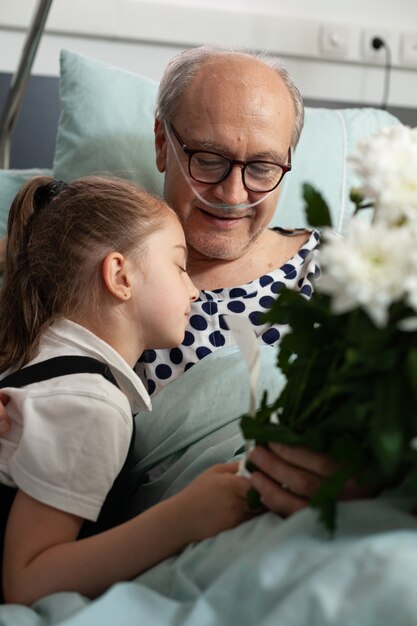 Little granddaughter hugging elderly grandfather visiting him in hospital ward