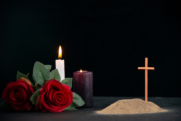 Little grave with candle and flowers as memory on dark surface