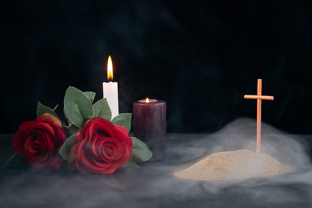 Little grave with candles and flowers as memory on dark surface