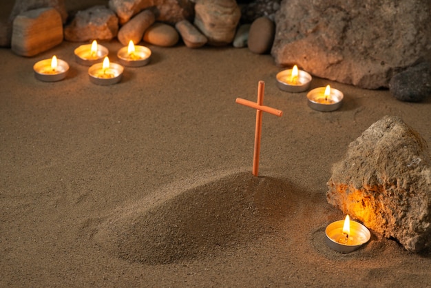 Free photo little grave with stones and burning candles around on sand funeral death