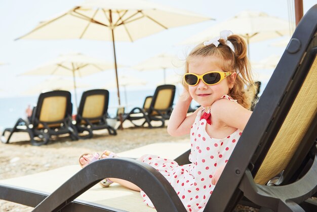 Little happy girl on the sunbeds by the sea