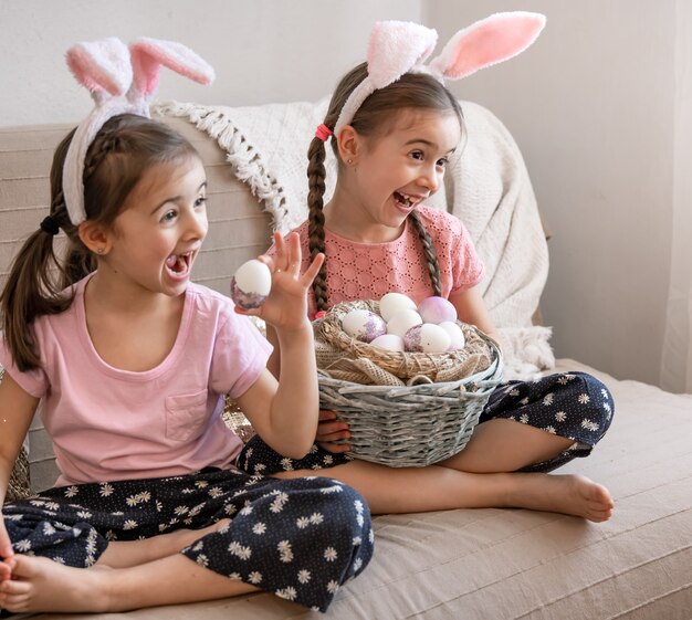 Little happy sisters with bunny ears pose with a basket of Easter eggs