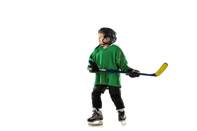 Little hockey player with the stick on ice court, white studio background. Sportsboy wearing equipment and helmet, practicing, training. Concept of sport, healthy lifestyle, motion, movement, action.