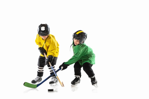 Piccoli giocatori di hockey con i bastoni sul campo da ghiaccio e la parete bianca dello studio