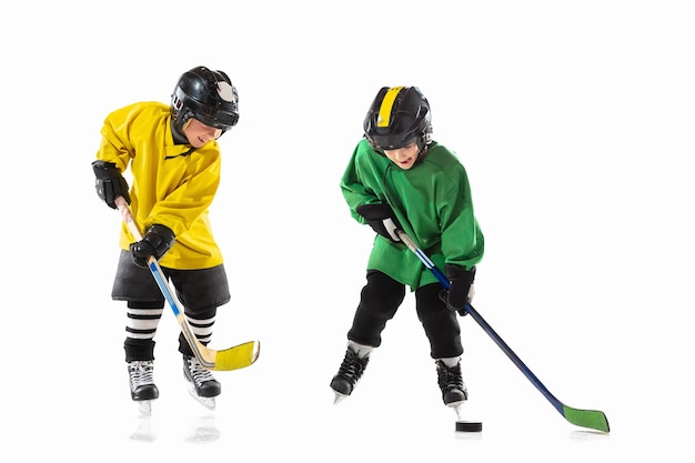 Little hockey players with the sticks on ice court and white  wall. Sportsboys wearing equipment and helmet practicing. Concept of sport, healthy lifestyle, motion, movement, action.