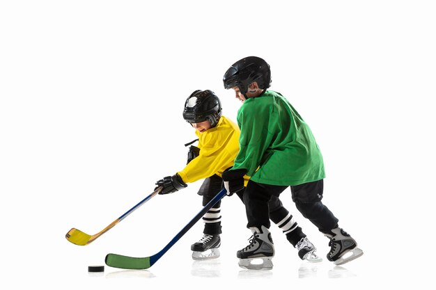 アイスコートと白い壁に棒を持った小さなホッケー選手。装備とヘルメットを身に着けて練習しているスポーツボーイ。スポーツ、健康的なライフスタイル、動き、動き、行動の概念。