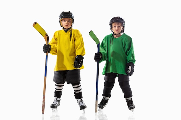 Free photo little hockey players with the sticks on ice court and white  wall. sportsboys wearing equipment and helmet practicing. concept of sport, healthy lifestyle, motion, movement, action.