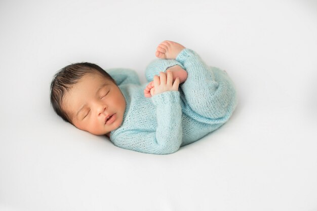 Little infant newborn laying on little white chair in blue crocheted pijamas