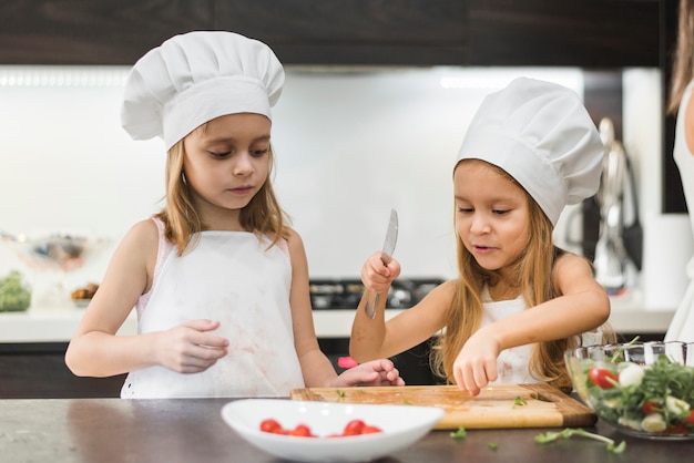 Little kid assisting her sister to cut vegetables with knife