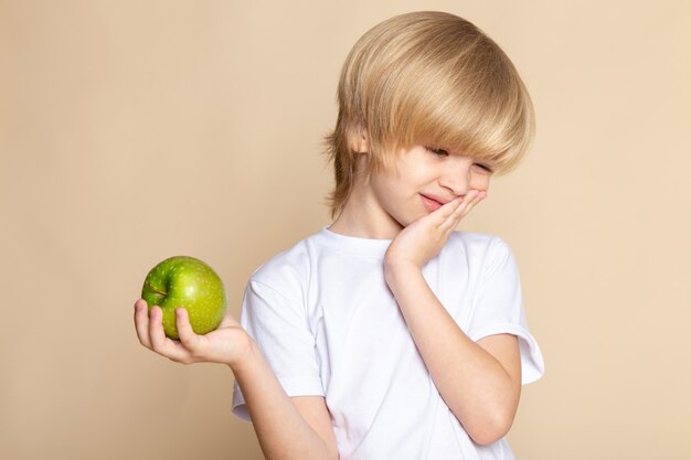 Free photo little kid blonde cute in white t-shirt holding green apple on pink wall