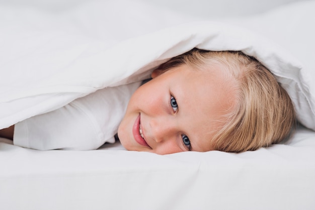 Little kid staying in bed while looking at the camera close-up