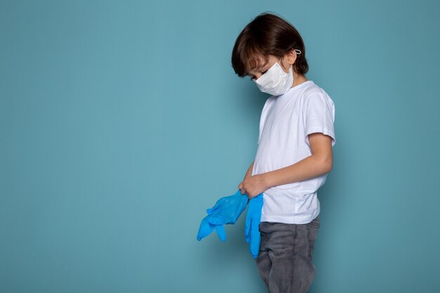 Маленький ребенок в белой защитной стерильной маске и синие перчатки в качестве защитной меры против коронавируса на синем