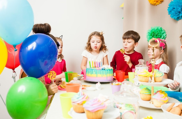 Маленькие дети празднуют день рождения. девушка загадывает желание перед тем, как задуть свечи на торте