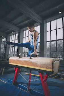 Little male gymnast training in gym, composed and active. caucasian fit little boy, athlete in sportswear practicing in exercises for strength, balance. movement, action, motion, dynamic concept