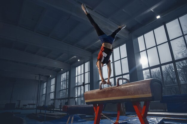 ジムでの小さな男性体操選手のトレーニング、柔軟でアクティブ。コーカサス地方の少年、スポーツウェアを着たアスリートが、強さ、バランスの練習をしている。動き、アクション、動き、ダイナミックなコンセプト。