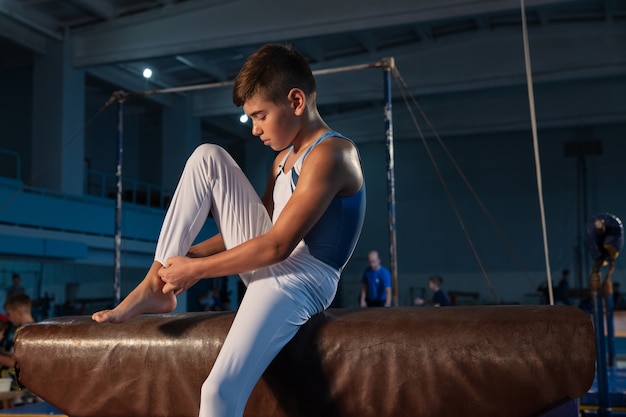 Маленький мужской гимнаст тренируется в тренажерном зале, гибкий и активный