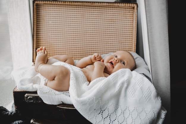 Foto gratuita piccolo neonato paffuto si trova su una soffice coltre bianca in una valigia aperta