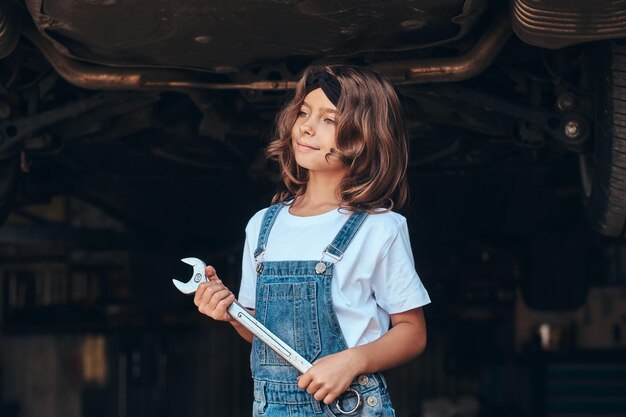 Little pretty girl is posing for photographer with tool at auto service workshop.